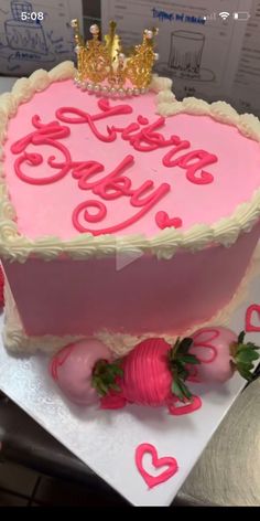 a pink heart shaped cake with strawberries on the bottom and two gold crowns on top