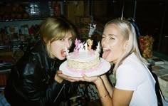 two women holding a cake with candles in their mouths and one is blowing out her tongue