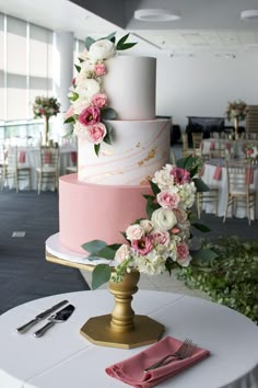 a wedding cake with pink and white flowers on top is sitting on a table in the middle of a banquet room