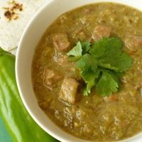 a white bowl filled with soup next to a green chili and pita bread on a table