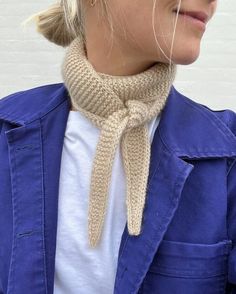 a woman wearing a blue jacket and a knitted cowgirl neck scarf in front of a white brick wall