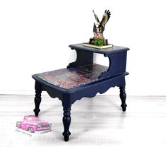 a small blue table with a pink car on it and an eagle figurine sitting on top