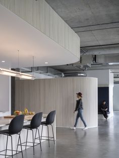 people are walking around in an office with high ceilings and white walls, along with black bar stools