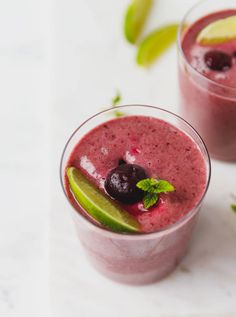 two glasses filled with smoothie and garnished with lime, blueberries, and cherries