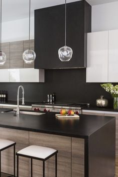 a modern kitchen with black counter tops and white cabinets, along with hanging lights above the island