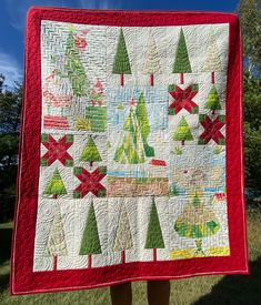 a person holding up a quilted christmas tree pattern on a red and white blanket