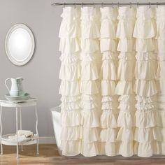 a white shower curtain with ruffles on it in front of a round mirror