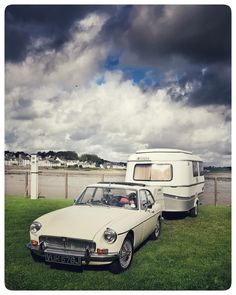 an old car parked next to a trailer on the grass near a body of water