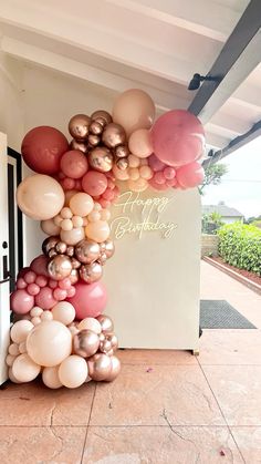 a large balloon arch with happy birthday written in gold and pink on the front door