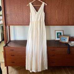 a white dress hanging on a wooden rack in front of a dresser with a framed photograph