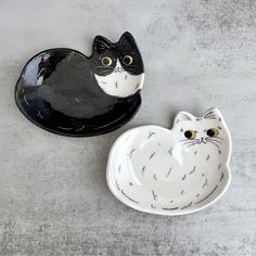 two black and white ceramic bowls with cats on them, one has yellow eyes while the other has an orange nose