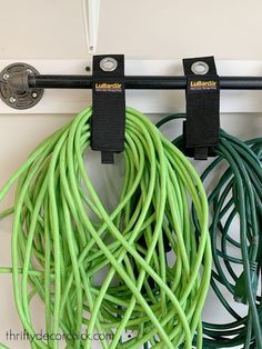 two green cords are attached to a hook on a white wall with a black handle