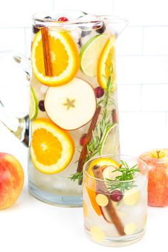 a pitcher filled with liquid next to sliced apples and oranges