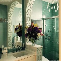 a bathroom with green tile and flowers in the vase on the sink counter next to the shower