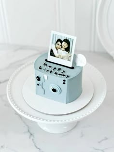 a cake with an old fashioned camera and two photos on it, sitting on a white plate