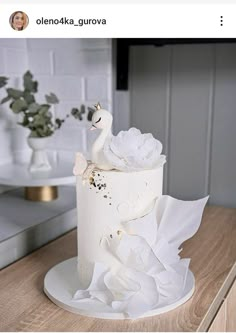 a white cake decorated with flowers and a swan on the top is sitting on a wooden table