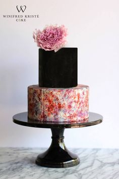 a three tiered cake with pink and black frosting on a marble table top