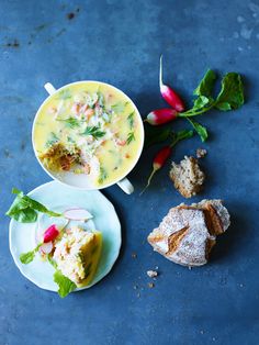 two plates with food on them next to some bread and radish sprigs