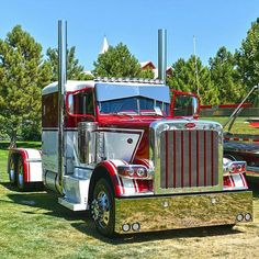 a red and white semi truck parked on top of a grass covered field