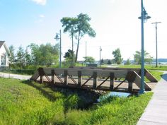 a wooden bridge over a small stream in the middle of a grassy area next to a house