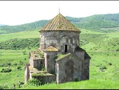 an old building in the middle of a green field with hills in the background and trees on both sides