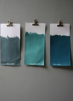 three different shades of blue and green on a gray wall with clipboards attached to them