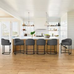 a kitchen with white walls and wooden flooring next to a dining room table surrounded by gray chairs