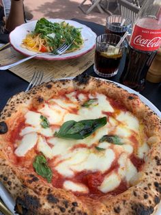 a pizza sitting on top of a white plate next to a salad and drink bottle