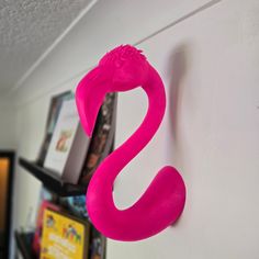 a pink flamingo shaped hook on the side of a white wall next to a book shelf