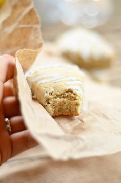 a person holding a piece of food with icing in their hand and some cookies on the other side