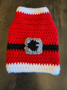 a red and white crocheted hat with a black circle on the center is sitting on a wooden table