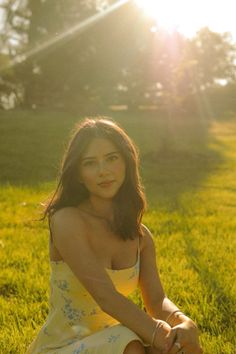 a woman in a yellow dress sitting on the grass with her hand on her knee