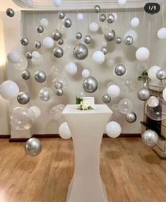 a room filled with lots of silver and white balloons hanging from the ceiling next to a table