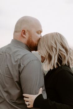 a man and woman standing next to each other in front of the ocean with their eyes closed