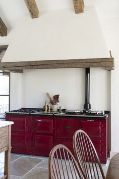 an old fashioned kitchen with red cabinets and wood beams on the ceiling, along with wooden dining chairs