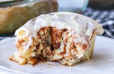 a cinnamon roll with icing sitting on a white plate next to a glass dish