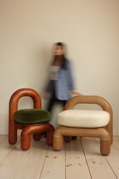 a woman walking past two wooden chairs and stools in a room with wood floors