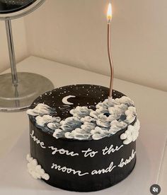 a black cake with white clouds and a single lit candle on top that says, i love you to the moon and back