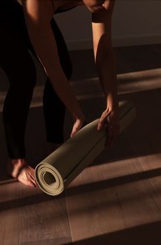 a woman rolling up a yoga mat on the floor with her hands and leg bent over it