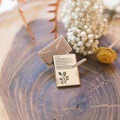 a small brooch sitting on top of a piece of wood next to a plant