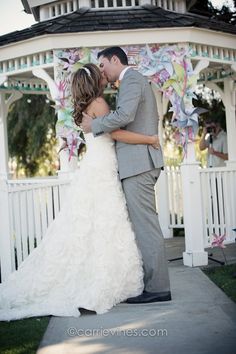 a bride and groom kissing in front of a gazebo