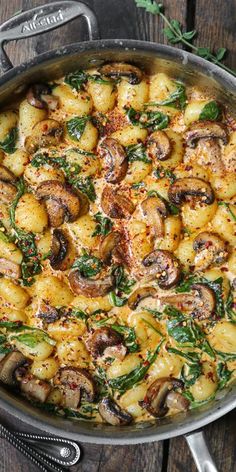 a pan filled with potatoes and mushrooms on top of a wooden table next to utensils