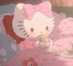 a hello kitty sitting on top of a bed holding a cup