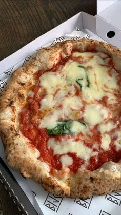 a pizza sitting on top of a box covered in cheese and tomato sauce with spinach