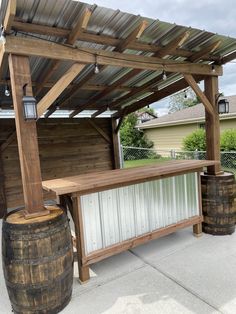 a wooden bench sitting under a pergolated roof next to two barrels on the sidewalk