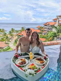 a man and woman posing for a photo while holding a heart shaped tray with food on it