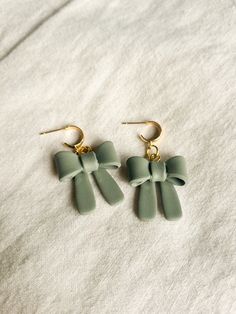 two pairs of green bow earrings on top of a white cloth covered bed sheet with gold ear wires