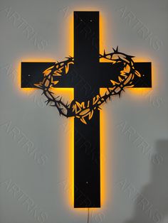 a cross with a crown of thorns on it is lit up against a white wall