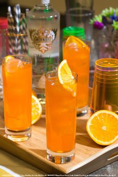 three glasses filled with orange juice on top of a wooden tray