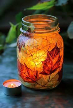 a lit candle sits next to a glass jar with leaves on it